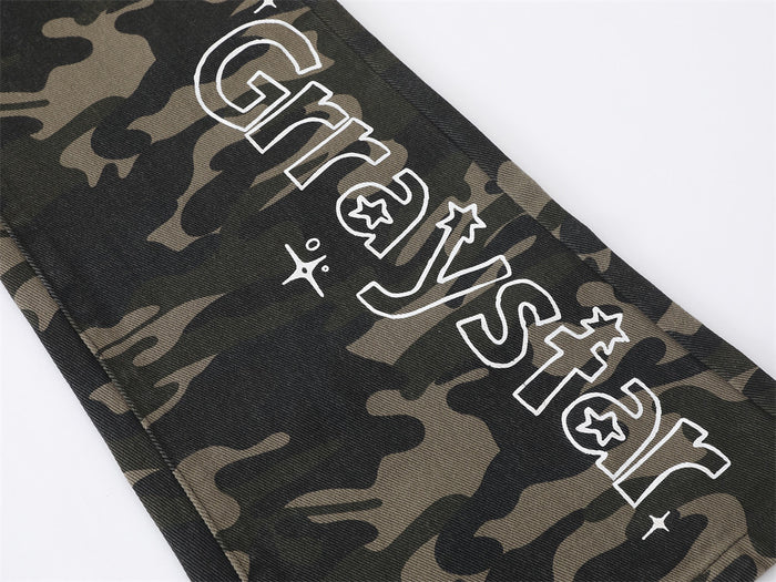 Close-up of outlined white letter print with star details on the camouflage jeans leg