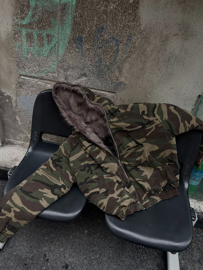 Camouflage faux fur-lined bomber jacket laid across a chair, showing the front, hood, and sleeves