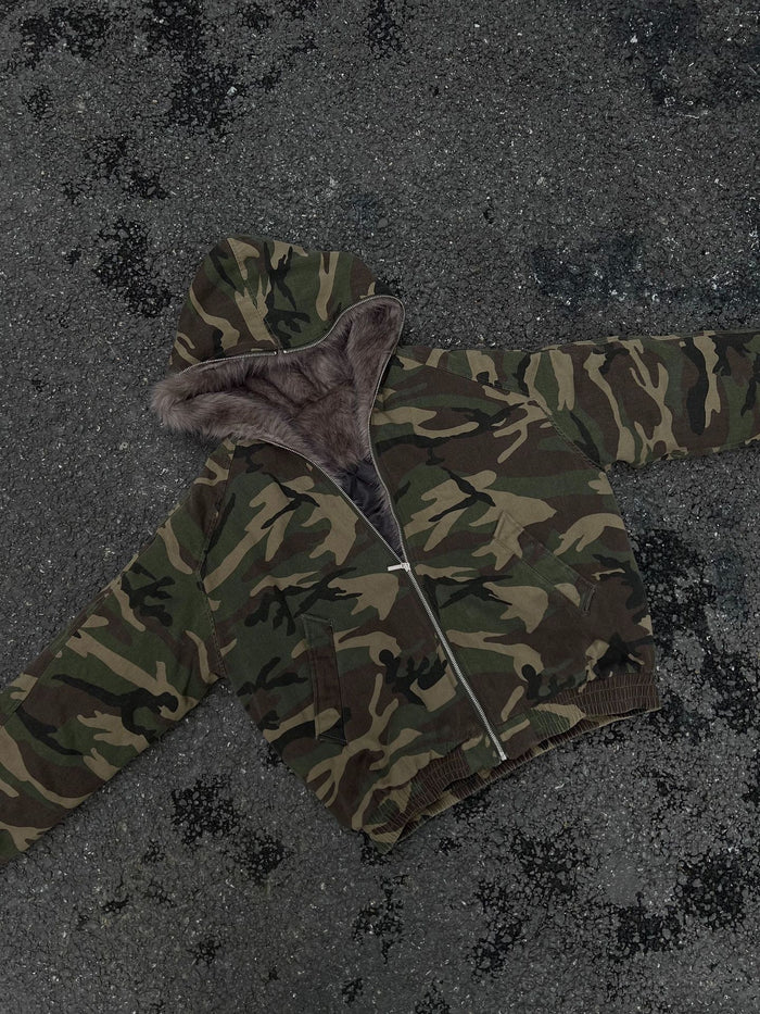 Camouflage bomber jacket spread on pavement, showing the hood, sleeves, front zipper, and ribbed hem