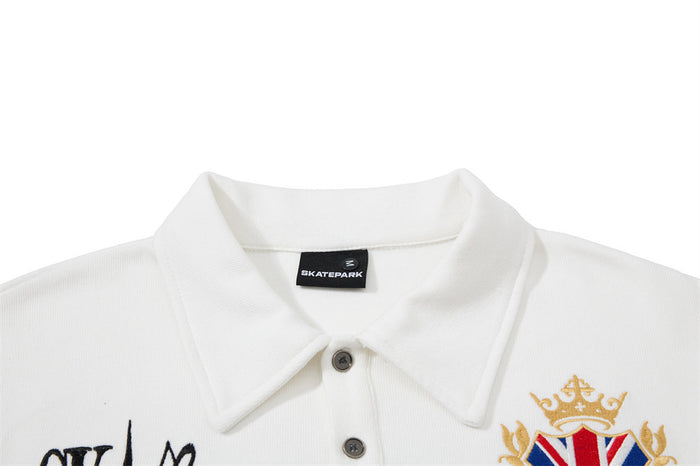 Close-up of the white polo shirt collar, button placket, woven label, and partial crowned Union Jack crest
