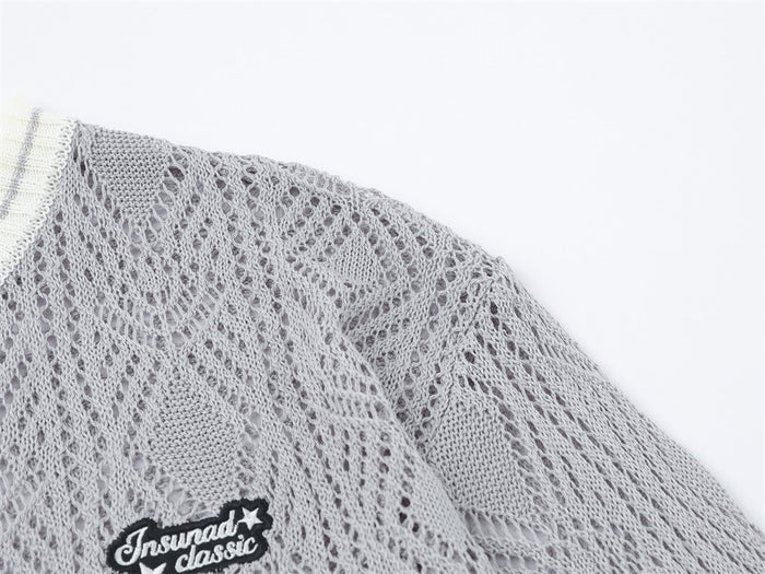 Close-up of gray open-knit cardigan shoulder and chest showing diamond texture and embroidered black patch