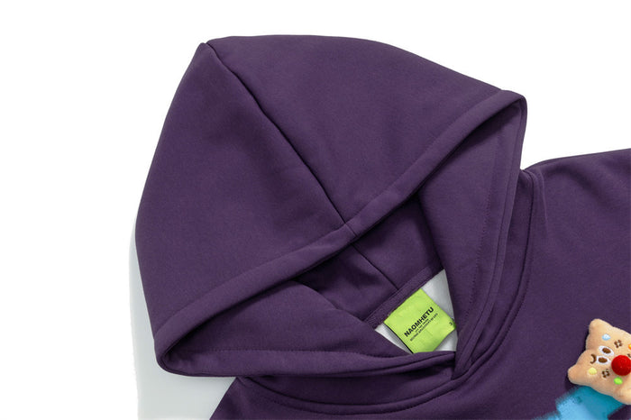 Close-up of the purple hoodie hood and neckline with a green label and small bear-shaped chest patch