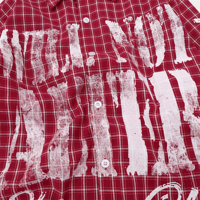 Close-up of distressed white block lettering printed across the red plaid shirt front