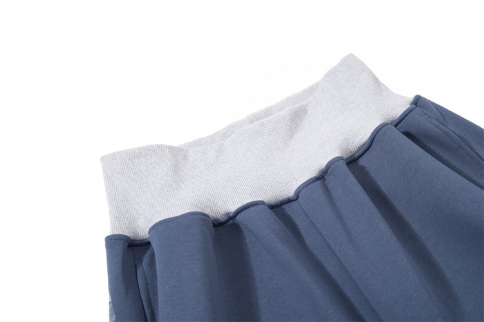 Close-up of slate blue sweatpants showing the white ribbed waistband, gathered seam, and smooth fabric