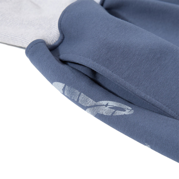 Close-up of slate blue pant fabric with a partial distressed white graphic and visible stitched seam
