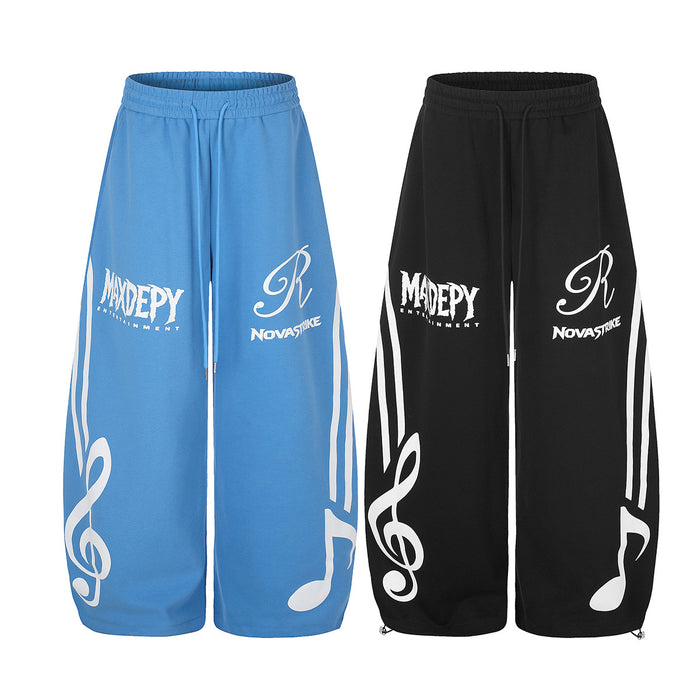 Blue and black wide-leg sweatpants shown from the front with white music note graphics and printed logos