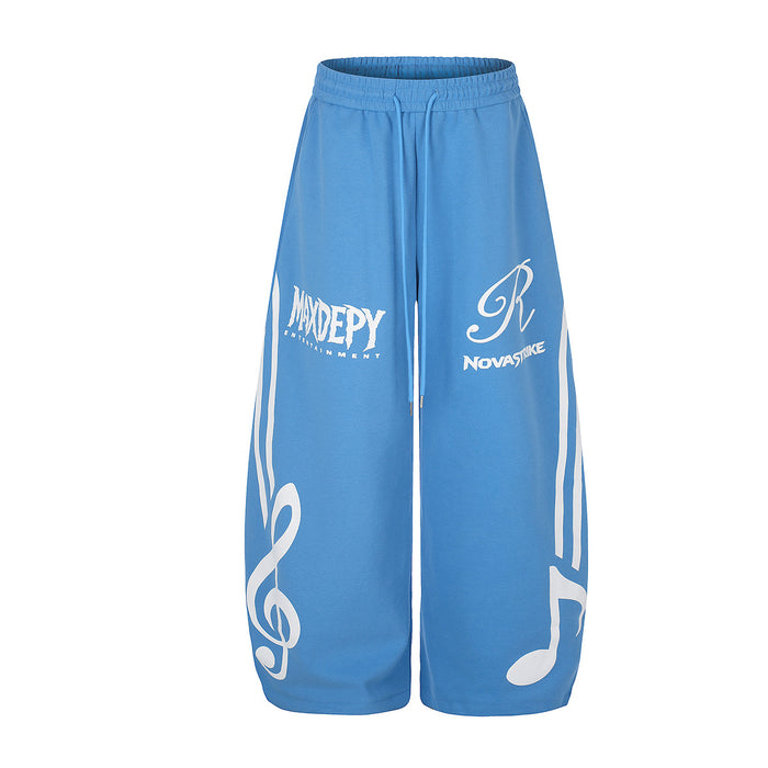 Blue wide-leg sweatpants shown from the front with white treble clef, note, stripe and logo graphics