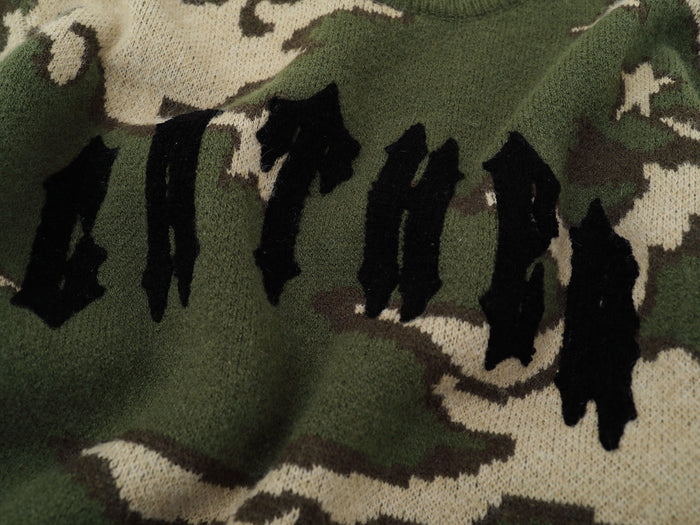 Close-up of black gothic logo knit on green camouflage sweater front