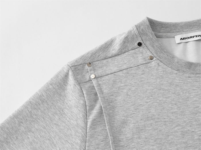 Close-up of light gray T-shirt shoulder panel with metal studs