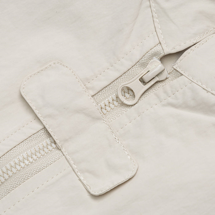 Close-up of the cream jacket’s front zipper, protective flap, pull tab, and fine woven texture