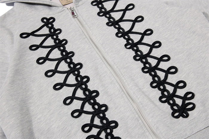 Close-up of black looped rope-lace detailing beside the front zipper on a light gray hoodie