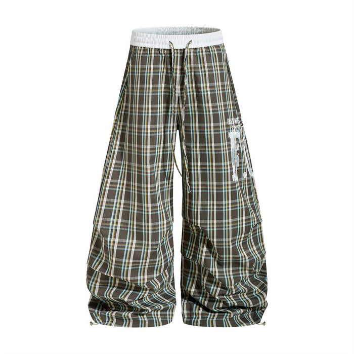 Oversized brown plaid wide-leg parachute pants with white elastic waistband and distressed letter graphics, front and back vi