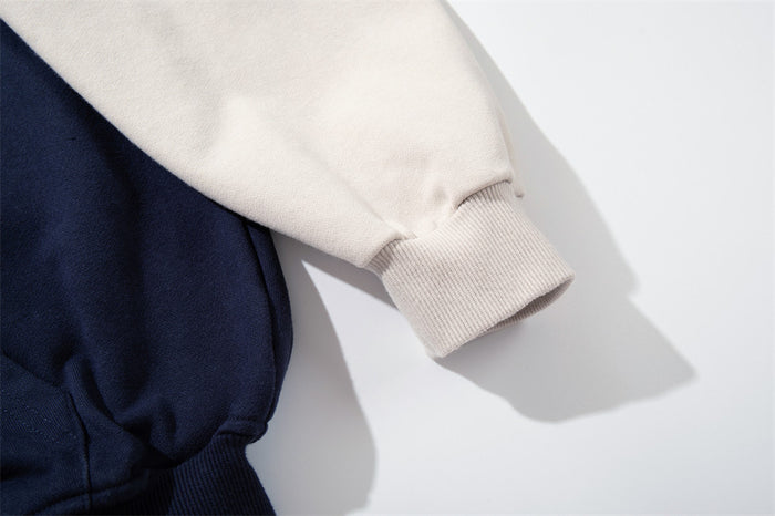 Close-up of a cream hoodie sleeve ending in a ribbed knit cuff beside the navy body