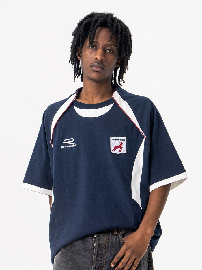 Oversized navy retro varsity football tee with white trim and crest patch on model against a white background