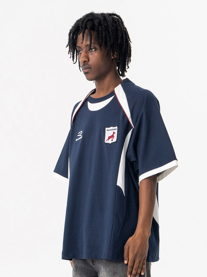 Oversized navy varsity football tee with white shoulder panels and retro crest detail on model