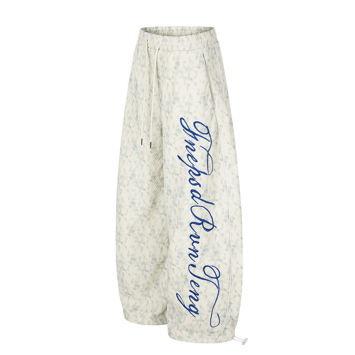 Side view of acid wash wide-leg sweatpants with blue script embroidery along one leg