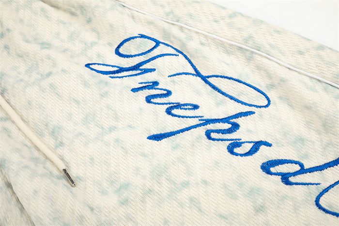 Close-up of blue script embroidery on acid wash sweatpants
