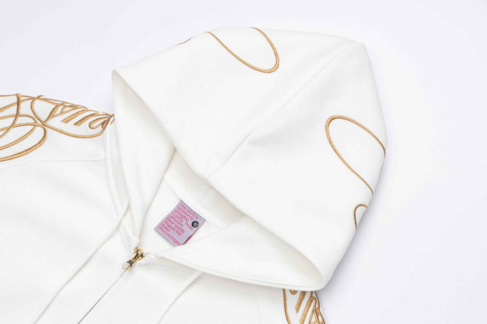 Close-up of a white hoodie hood showing gold curved embroidery, inner label, and soft fabric