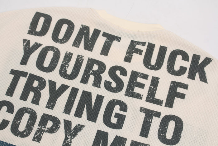 Close-up of distressed black slogan print on cream waffle fabric