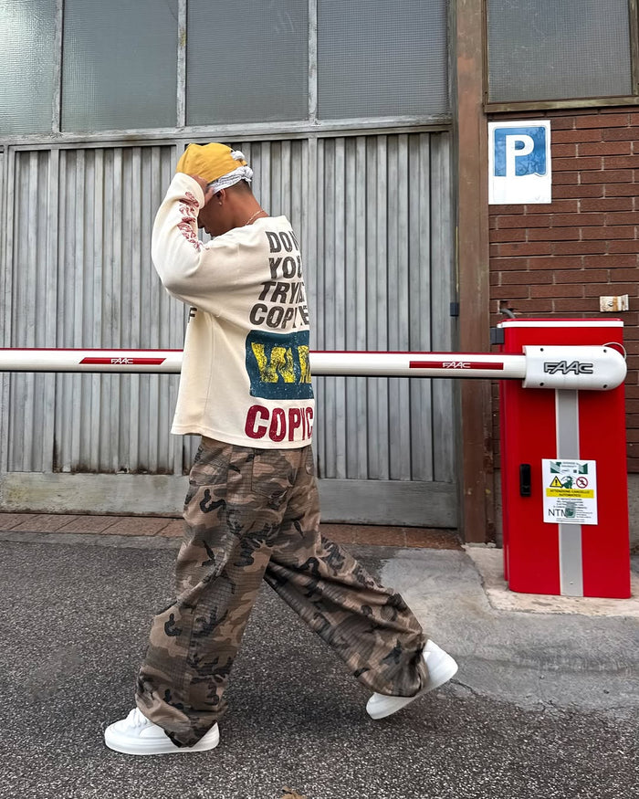 Side view of cream graphic long sleeve shirt and wide camo pants on model
