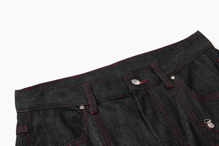 Close-up of black denim waistband with belt loops, silver button, and red contrast stitching