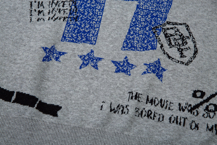 Close-up of front hem on gray knit sweater with blue stars and black printed text