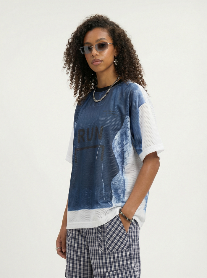 Model wearing a blue-and-white mesh jersey graphic tee with RUN print, styled with plaid cargo pants and sunglasses