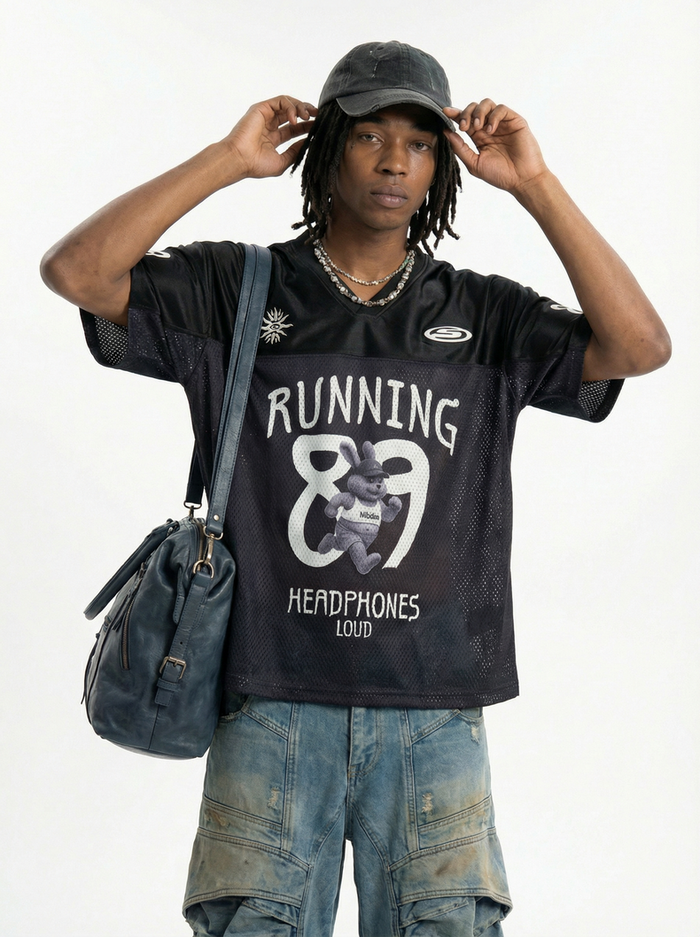 Man wearing black Running 89 mesh jersey with graphic print, cap, cargo pants, and shoulder bag against white background