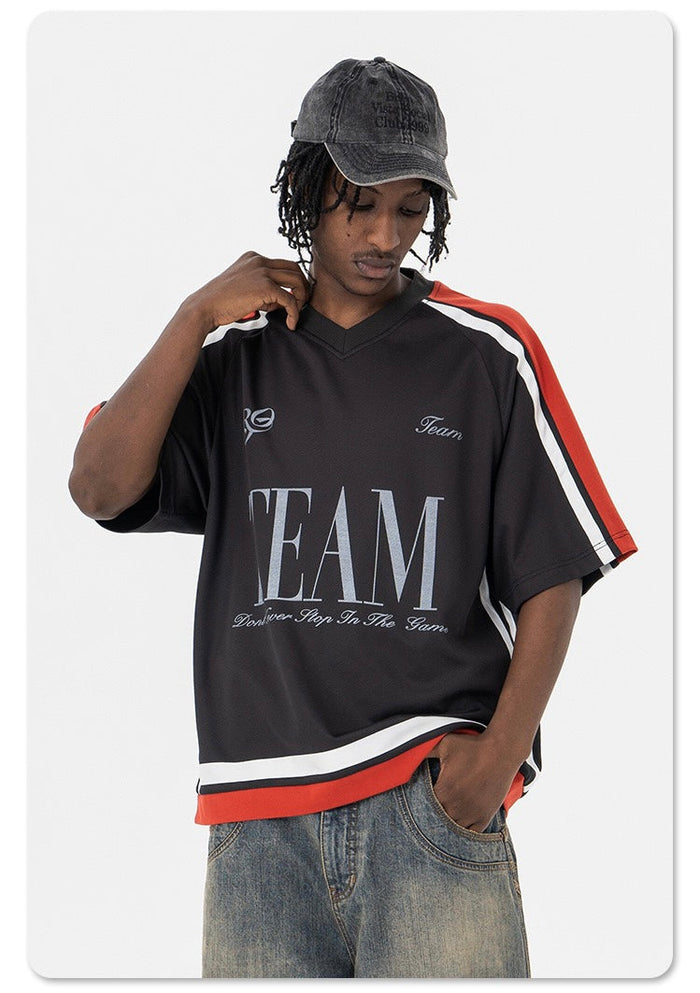 Oversized black varsity mesh tee with red and white striped sleeves and bold TEAM graphic, styled with baggy jeans and cap
