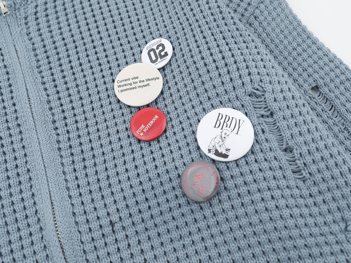 Close-up of light blue cardigan front with decorative badge pins and distressed knit holes