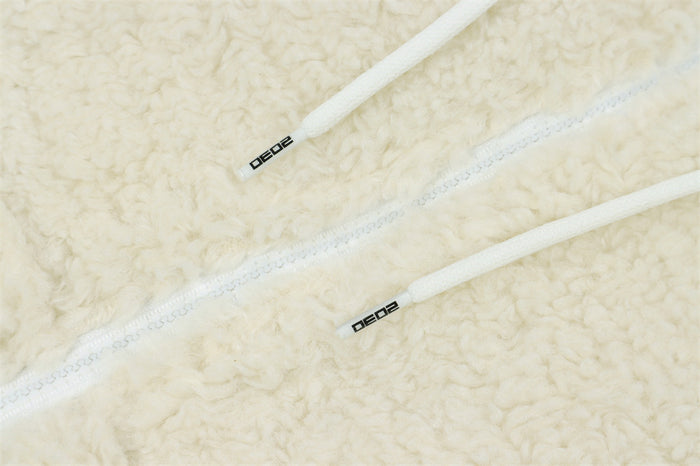 Close-up of white hoodie drawstrings with black printed ends beside the front zipper