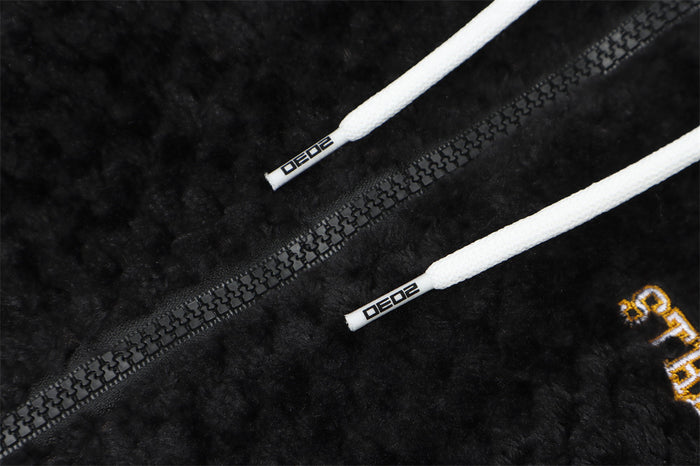 Close-up of the black sherpa hoodie showing the zipper, white drawstring tips, and partial chest embroidery