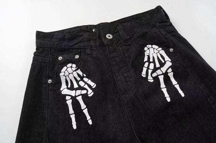 Front upper section of black denim pants with white skeleton hand prints near the pockets