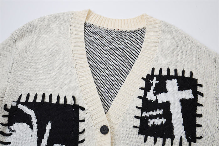 Close-up of cream cardigan V-neck showing ribbed trim, black patch graphics, contrast knit texture, and front button
