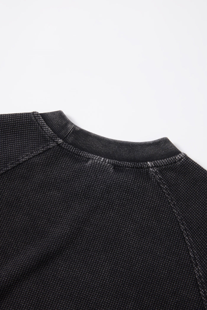 Close-up of a black textured crewneck T-shirt with ribbed collar against a clean white background