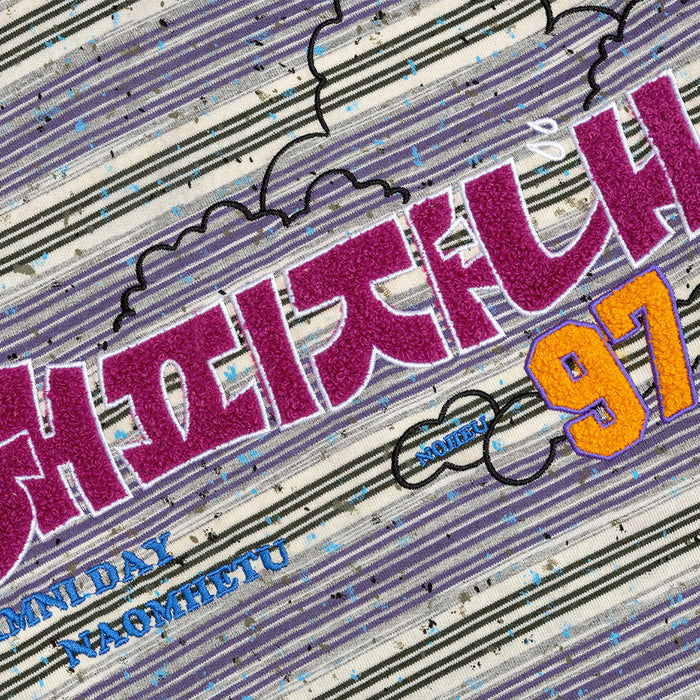 Close-up of the shirt chest graphic featuring magenta embroidered lettering, blue text, and orange numerals