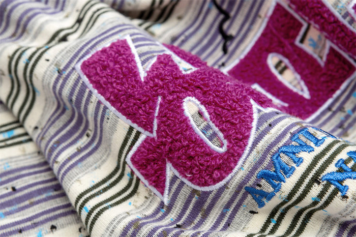 Detailed close-up showing raised magenta embroidery and blue lettering over the striped shirt fabric