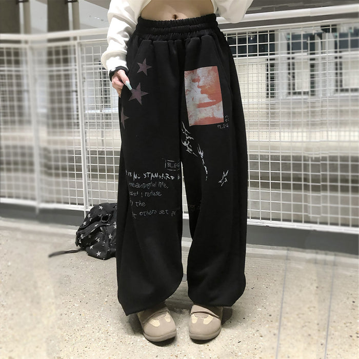 Black wide-leg sweatpants worn on a model, with star motifs, red graphic patch, and white text prints