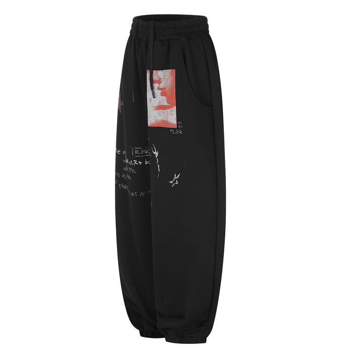 Angled side view of black wide-leg sweatpants showing the curved pocket, red patch, and scattered graphics