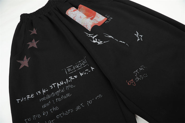 Close-up of black sweatpants featuring star motifs, a red rectangular patch, white script, and scattered graphic marks
