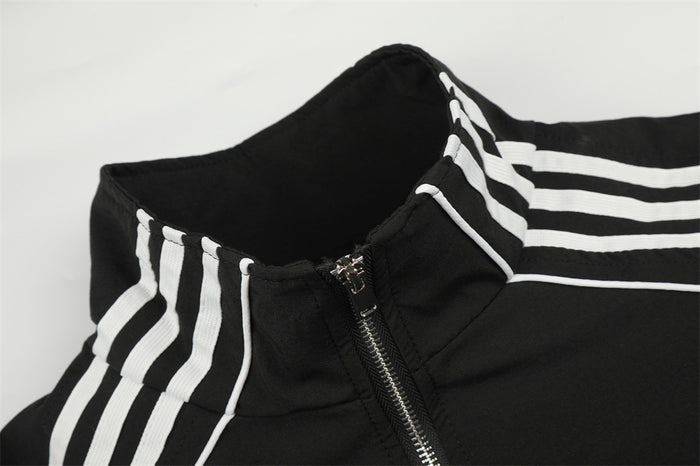 Close-up of the black track jacket mock neck, triple white stripes, piping, and metal zipper