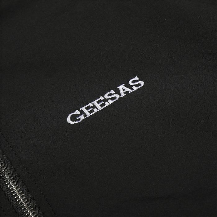 Close-up of the embroidered white GEESAS logo on the black track jacket chest
