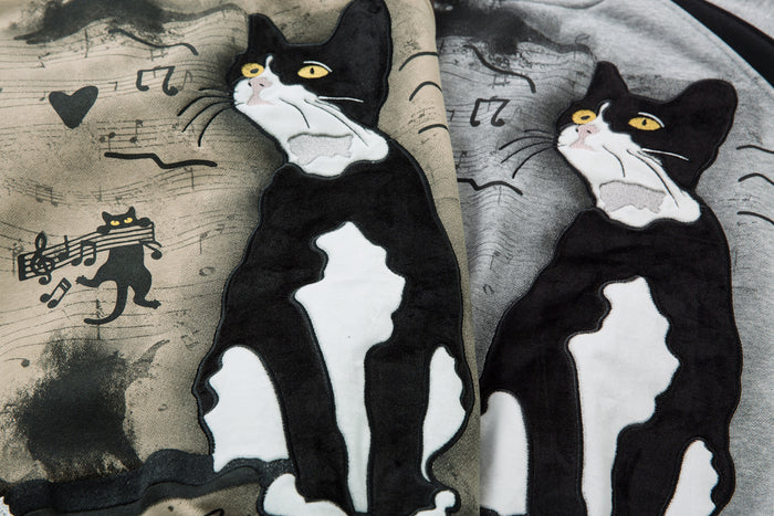 Close-up of the tuxedo cat graphic on beige and gray sweatshirt fabric with hearts and musical notes