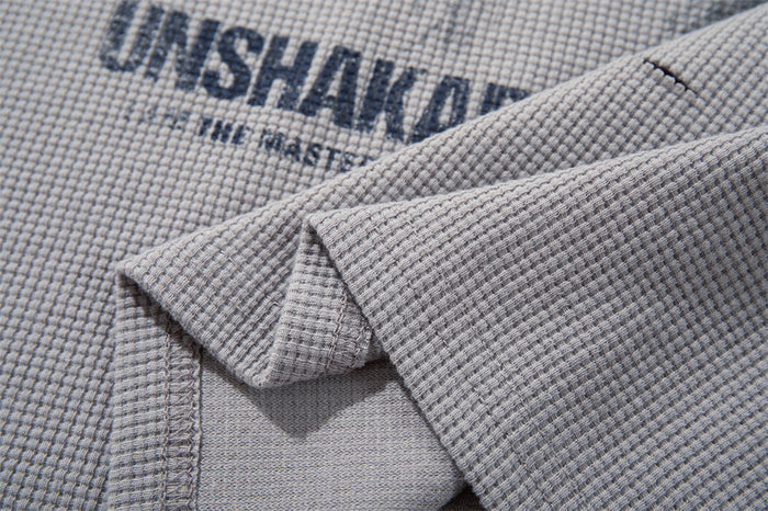 Close-up of printed front graphic on light gray waffle knit T-shirt with folded sleeve