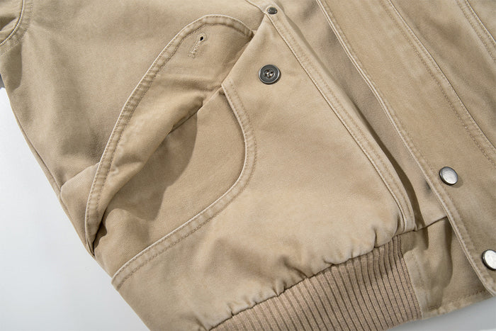 Close-up of a washed khaki bomber jacket front cargo pocket with flap, snap button, curved opening and stitched seams