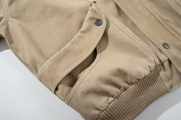 Close-up of the washed khaki jacket's open cargo pocket flap, front seam and ribbed waistband