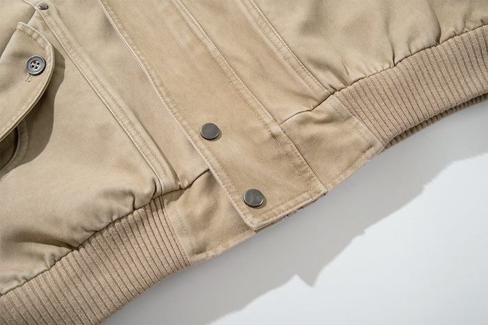 Close-up of the washed khaki bomber jacket's lower front snap closure, seam details and ribbed hem