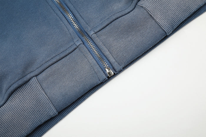 Close-up of the hoodie lower front showing the zipper base, pocket seam, and ribbed waistband