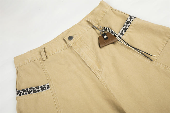 Close-up of beige pants waist with carabiner charm and leopard trim at the pocket