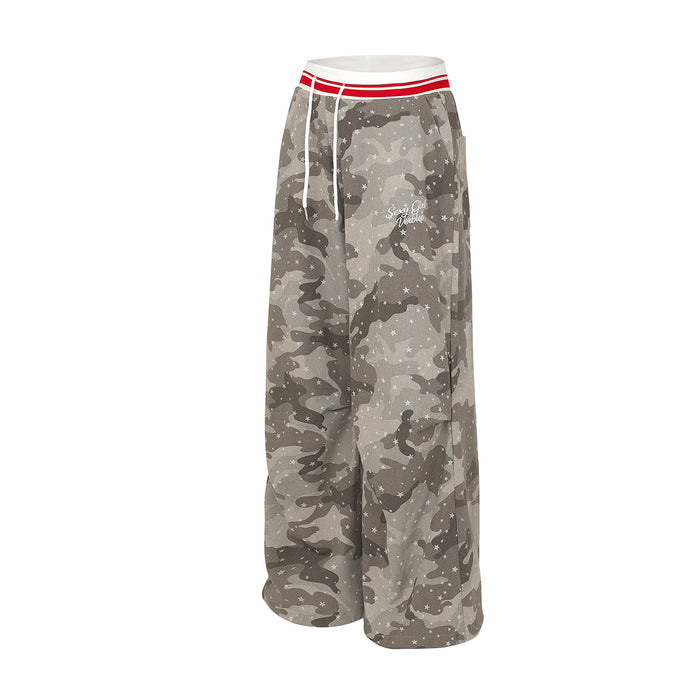 Angled side view of wide-leg gray camouflage pants with scattered white stars and a red-striped waistband